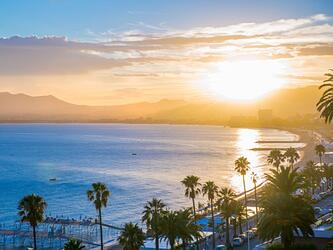 sunset over Cannes seafront with palm trees in foreground, and sea and mountains on the horizon